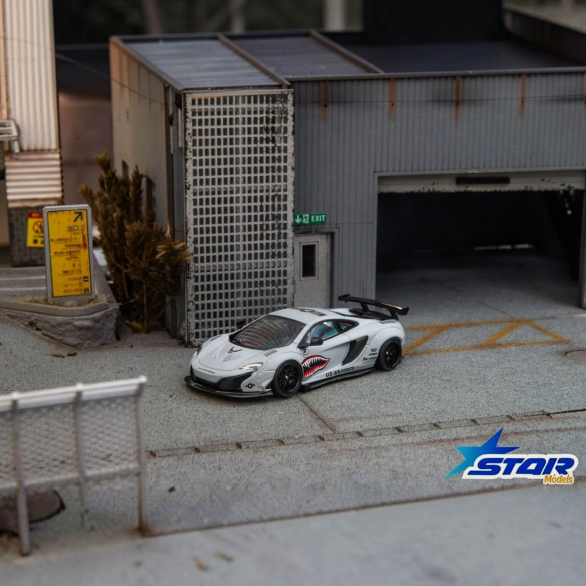 Star Models McLaren 650S Wide-Body Air Force Grey Shark Mouth 1:64 diecast, front three-quarter in a garage diorama
