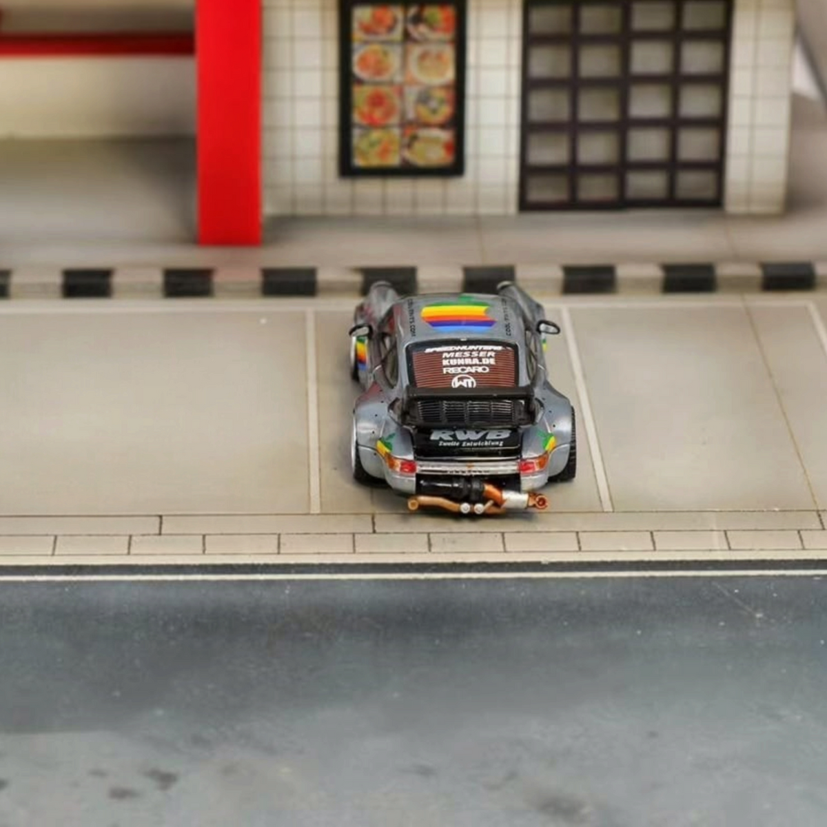 SW RWB Porsche 964 High Wing - Apple Racing Livery 1:64 diecast model, rear view with rainbow roof logo in diorama