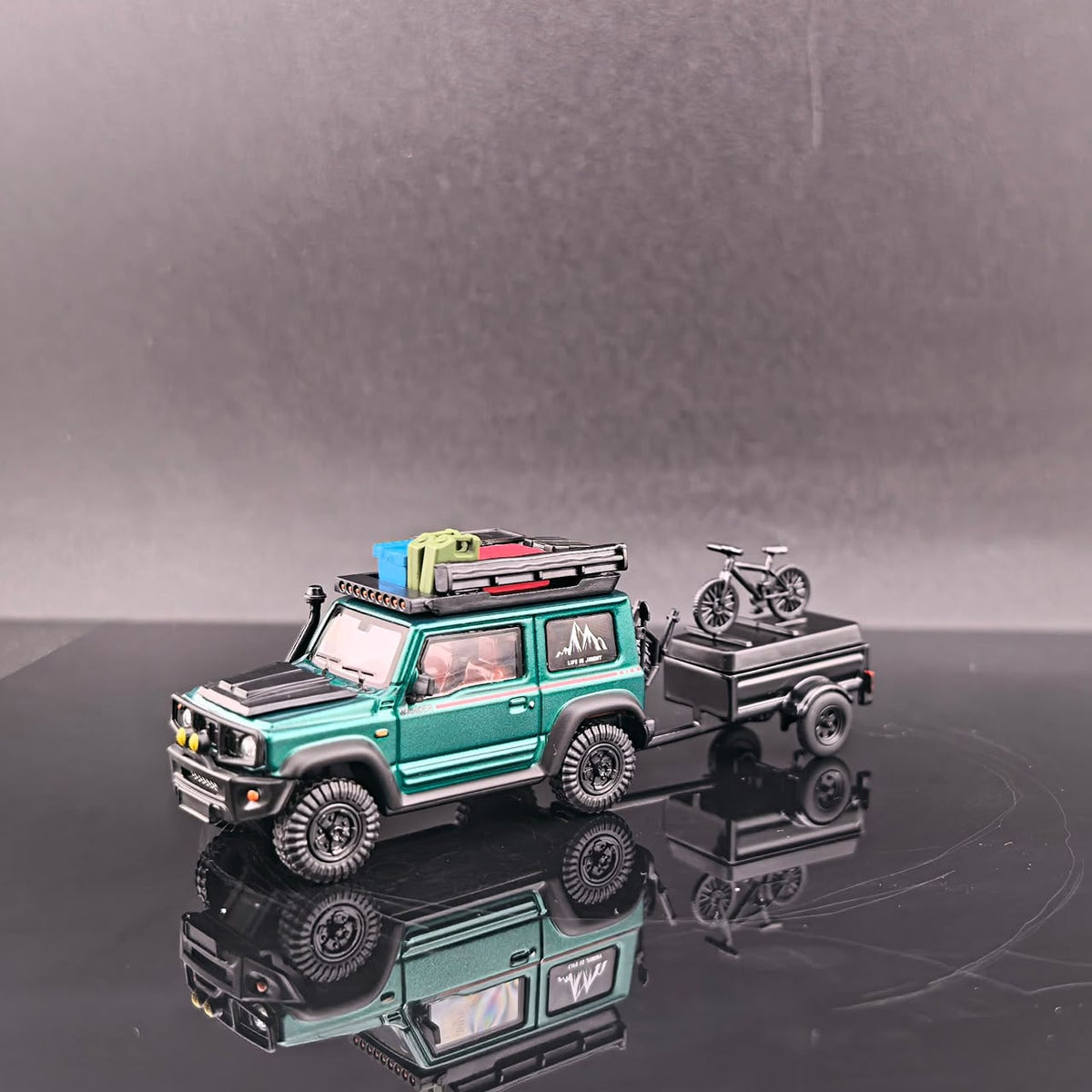 Front three-quarter view of the green Jimny with roof gear and the trailer carrying a bike