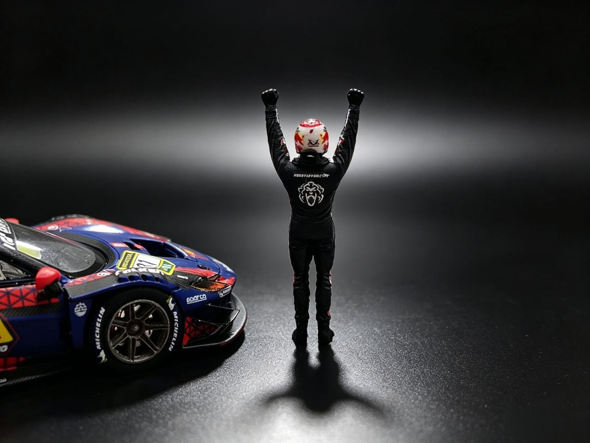 Driver figure in a black race suit and Red Bull helmet, arms raised, seen from behind beside the MechSpeed 296GT3 1:64 in blue Red Bull livery