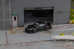 Star Models 1:64 Porsche 997 widebody in gloss black, front three-quarter view in a loading-dock diorama