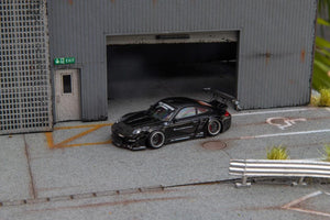 Star Models 1:64 Porsche 997 widebody in gloss black, front three-quarter view in a loading-dock diorama