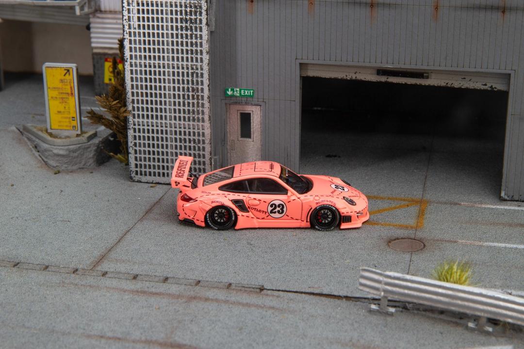 Star Models 1:64 Porsche 997 widebody in Pink Pig livery with number 23 roundel, full side profile showing the widebody fenders