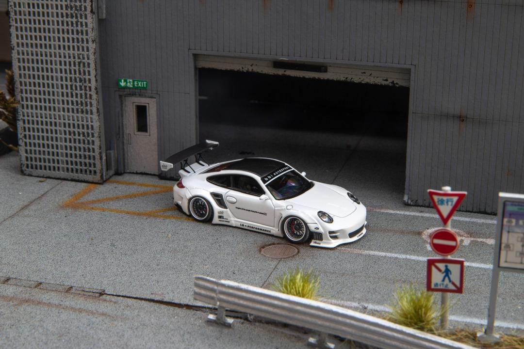 Star Models 1:64 Porsche 997 widebody in white with a carbon roof, front three-quarter from the right showing the wide arches
