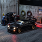 TimeMicro 964 RWB 1:64 in black lit up in a garage diorama, mechanic figures stacking tyres behind it, red light glowing on wet asphalt