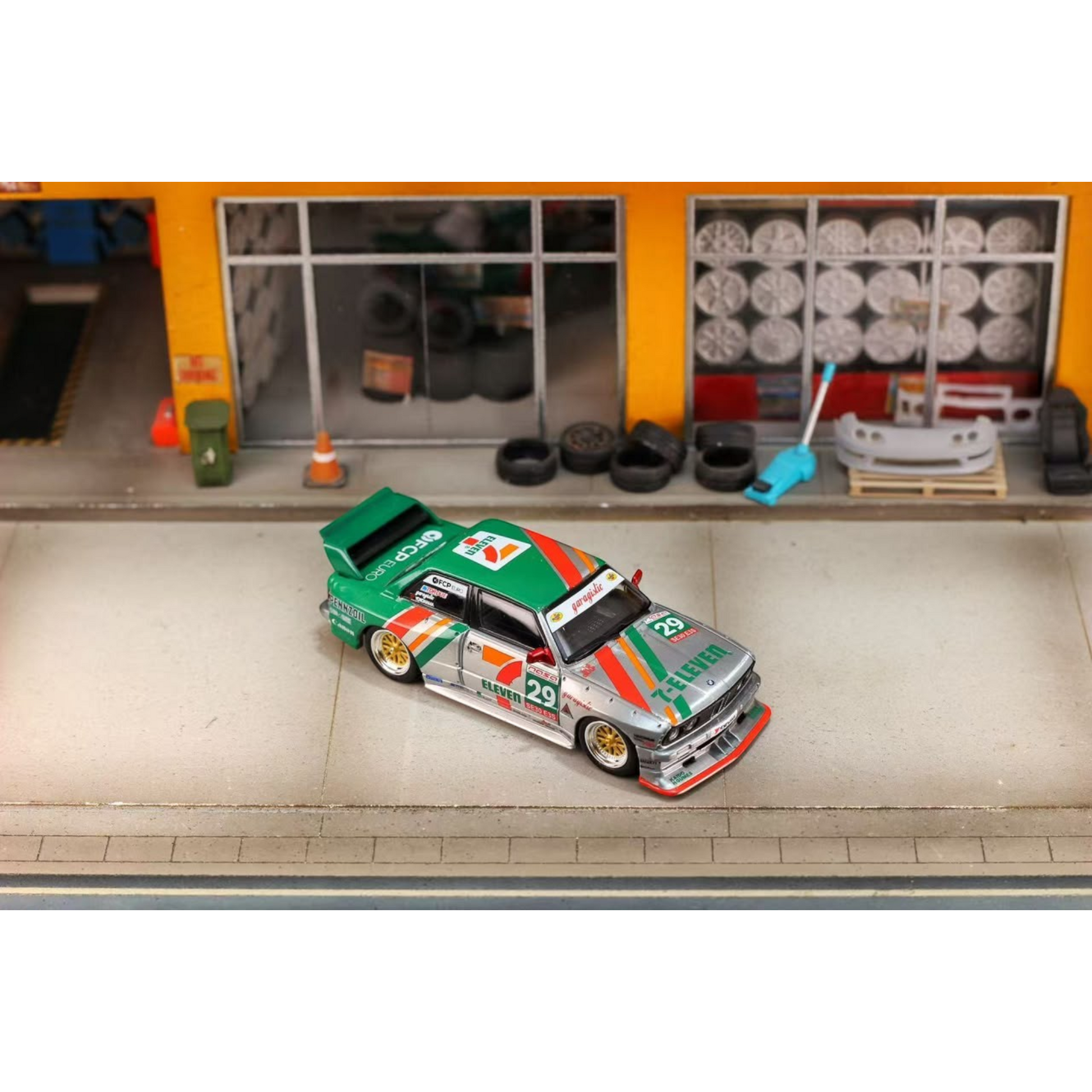 Lot57Supplies Diecast Shop GHOST PLAYER BMW E30 1:64 scale diecast model car in 7-Eleven livery parked in a garage diorama